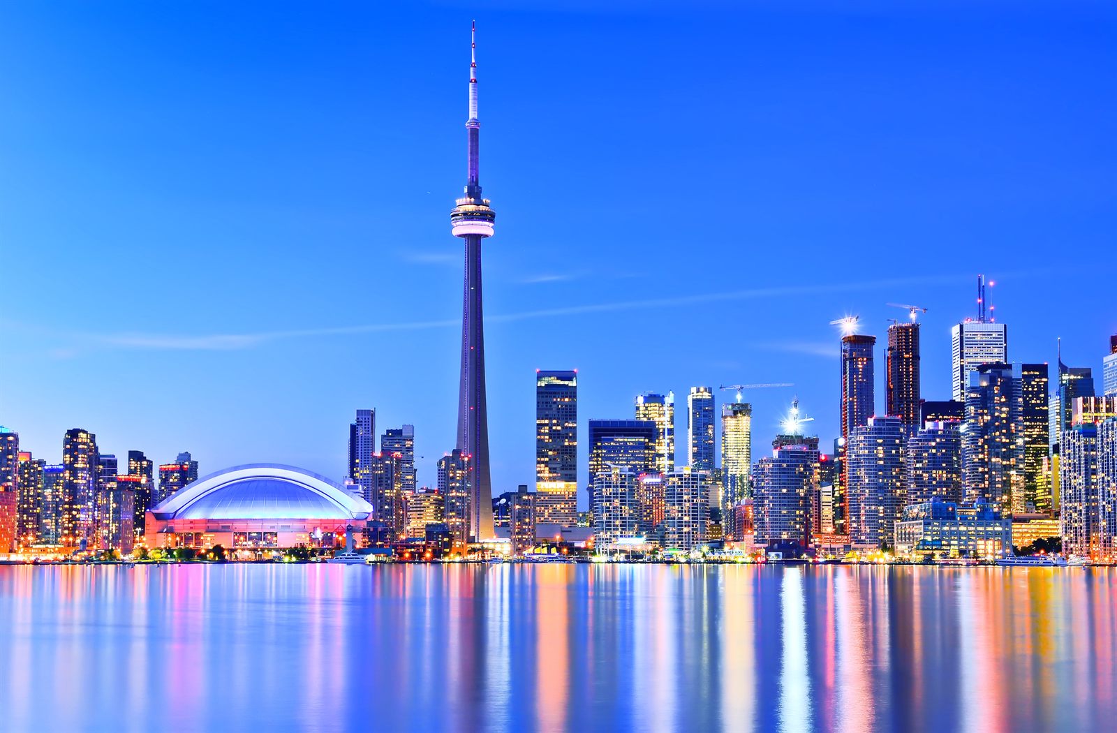Toronto skyline at night with the CN Tower and a domed stadium lit up across the water