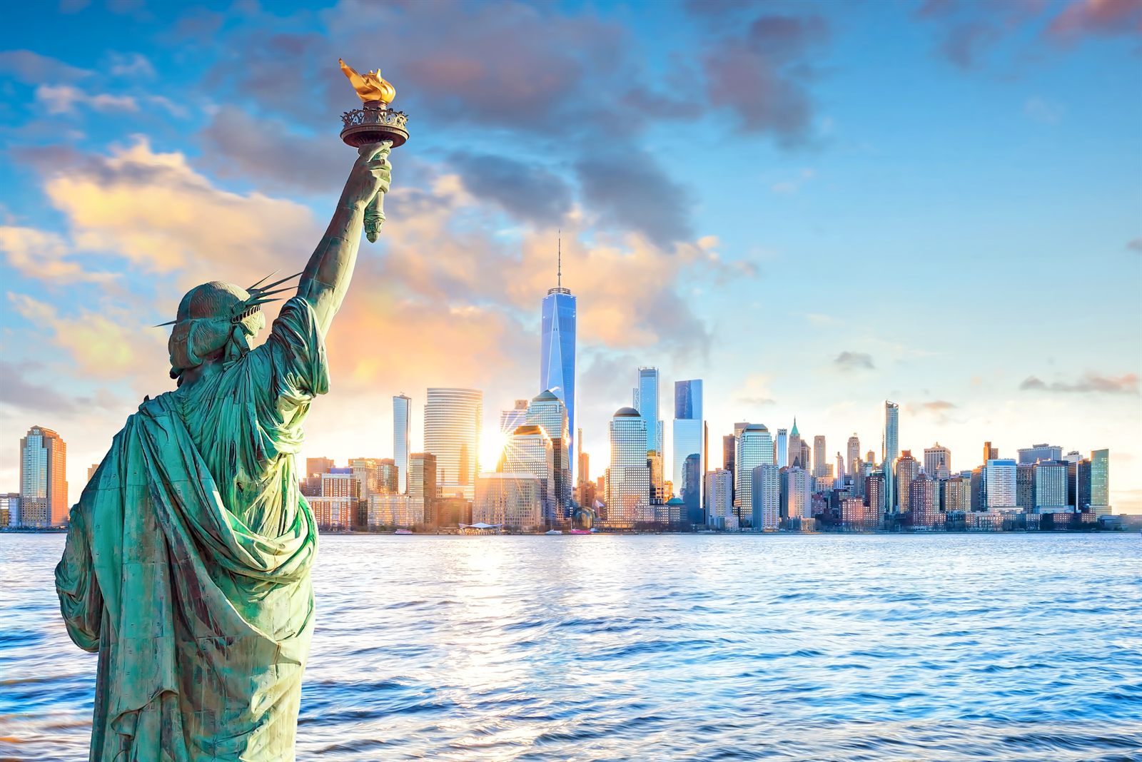 Statue of Liberty raising her torch at sunset with the Lower Manhattan skyline across the harbor, a backdrop to daily travel industry news